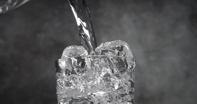 Water pouring into glass with ice cubes in slow motion on black background