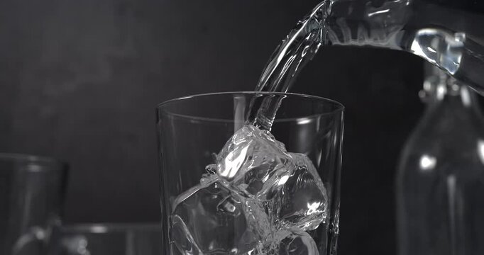 Water pouring into glass with ice cubes in slow motion on black background
