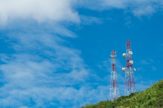 Communication towers and antennas rising above a forested hillside under blue sky, telecommunications infrastructure for wireless signal, mobile network and data transmission. Mobile network coverage.