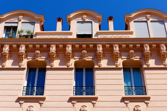 Pink Belle Epoque building facade with carved corbels and wrought-iron balconies, Cannes French Riviera, France.