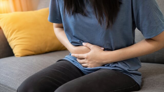 Close up of woman holding stomach in pain while sitting on sofa at home