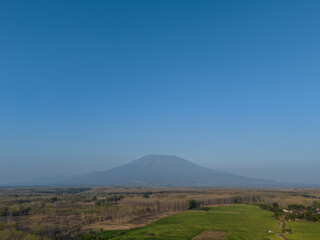 Fototapeta premium Scenic view of a majestic mountain under a clear blue sky, with lush green fields and rural landscape in the foreground.