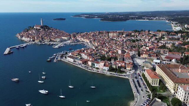 Aerial view of Rovinj historic old town in Croatia, featuring red tiled rooftops, St. Euphemia Church, marina, boats and the beautiful Adriatic coastline.