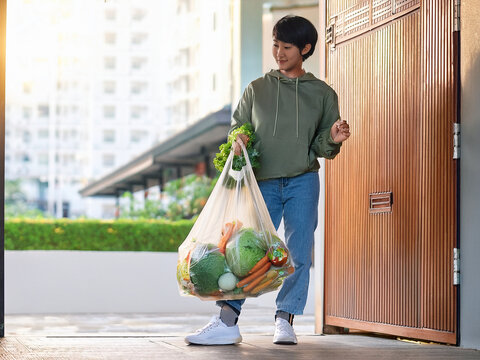 女性が買い物袋に野菜を抱えて玄関から出てくる
