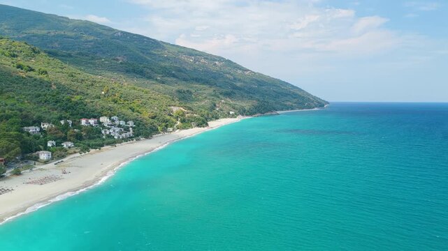 Aerial view of Chorefto Beach along the lush green slopes of Mount Pelion, Greece. The coastline stretches into the distance under a partly cloudy sky, with no people visible on the beach