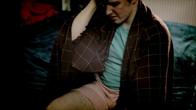 Sick guy with cold, flu or virus illness with cough and running nose lying in bed and using tissues. Sneezing ill guy at home. Man and health