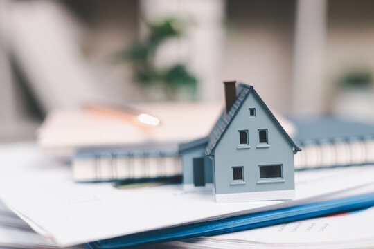 Miniature house on loan paperwork and notebooks represents mortgage documentation, property finance, home buying preparation, lender review, budgeting, affordability,