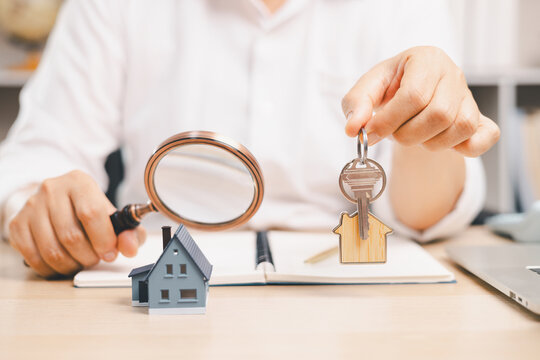 Professional holding house keys beside a magnifying glass and miniature home symbolizes property search, home inspection, buyer research, real estate verification, key handover,
