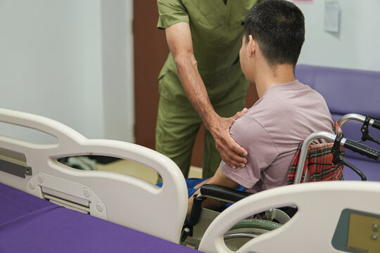 Healthcare worker supporting a disabled man in a wheelchair in a hospital room, providing compassionate patient care, assistance and emotional support during illness and recovery