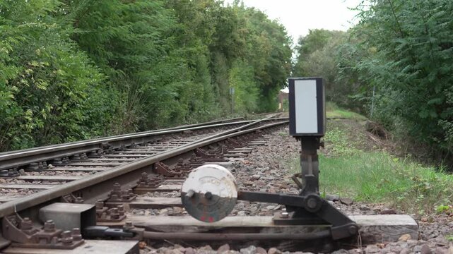 Cinematic tracking shot passing a railway switch indicator beside train tracks in a green rural landscape
