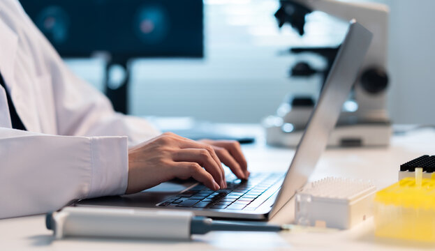 Close-up of a laboratory scientist typing research data on a laptop beside a micropipette and sample racks, representing digital documentation, biomedical analysis, and modern laboratory workflow.