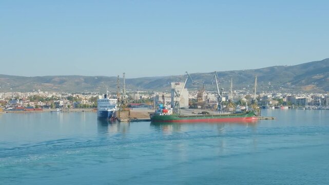 The commercial port of Volos in Thessaly, Greece, featuring cargo ships, cranes, and waterfront buildings with mountains in the background