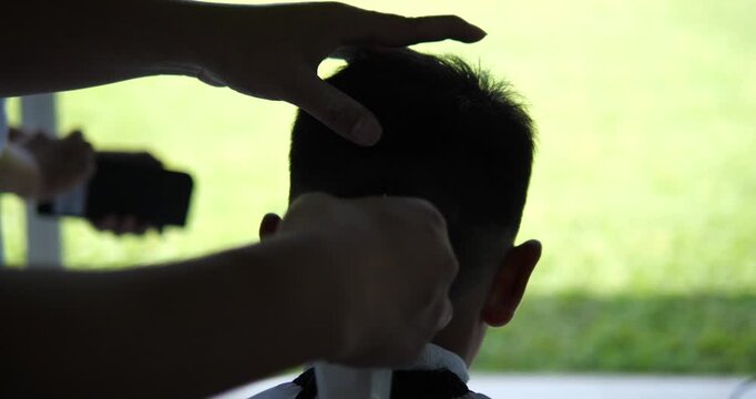 Back view of barber trimming boy short hair with clipper outdoors