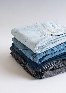 A stack of neatly folded denim jeans in various shades of blue and grey arranged on a white background.