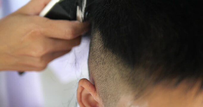 Close up of barber using electric hair clipper to cut man short hair in barbershop