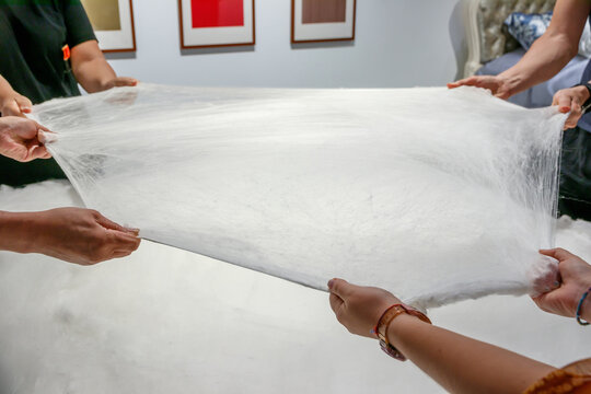 Multiple hands pull and stretch a fragile white sheet of raw silk in a hands-on chinese luxury workshop, showcasing traditional artisan technique