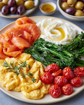 Vibrant breakfast plate with scrambled eggs and fresh herbs. Roasted tomatoes add bright color and tangy flavor. Smoked salmon slices offer rich, delicate taste. Crisp broccolini gives texture