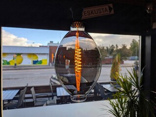 Glowing vintage decorative Edison bulb hanging indoors near window overlooking street © Dim