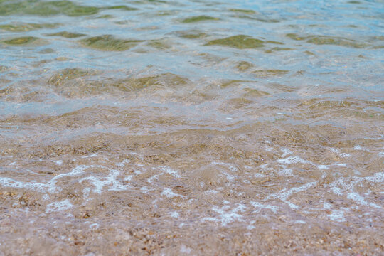砂底が透ける浅瀬に広がるさざ波と白い泡