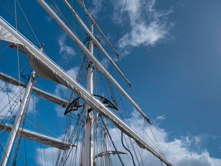 Masts and yards of a square rigged tall ship with furled sails stand out against a bright blue summer sky. © Victor