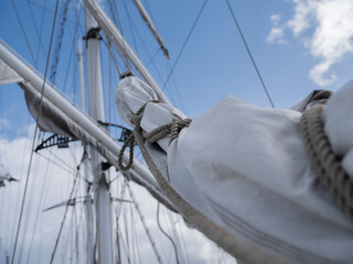 A furled sail lashed to the yard of a tall ship with rope and a hanging loop, rigging and clouds soft behind it. © Victor