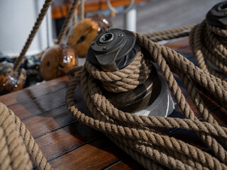 A black deck winch with natural fibre rope coiled around it on the varnished wooden deck of a traditional sailing ship in the sun. © Victor