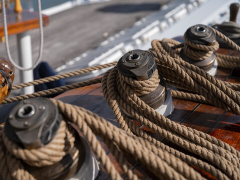 Three winches with coiled rope on the glossy teak deck of a classic sailing yacht, warm wood tones and shallow depth of field.