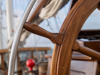 Close-up of the polished hardwood wheel of a sailing ship with its steel guard, the deck behind softly out of focus. © Victor