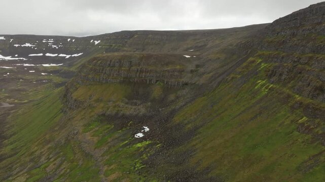 Aerial drone shot of rugged, green mountains and a table mountain in Hornstrandir nature reserve on Iceland, panning left over the landscape.