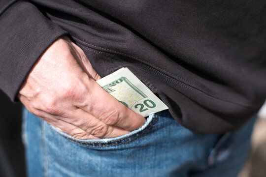 A man puts US dollars into the pocket of his jeans.
