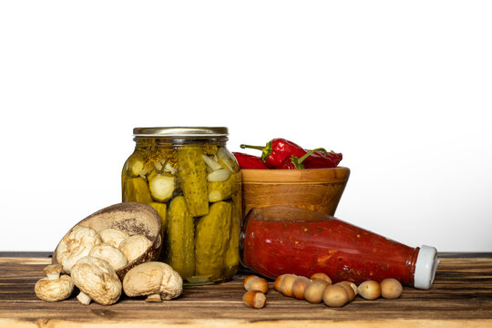 Culinary still life with pickled cucumbers, tomato sauce, mushrooms, and peppers on wooden table against white background   