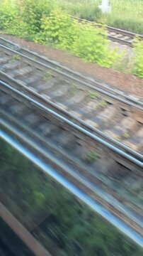 Railway tracks pass a moving train through green vegetation. Motion blur conveys speed and travel from a window. Transportation background for journey and progress concepts.