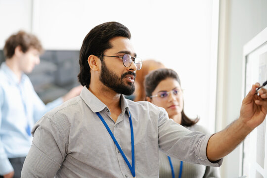 Diverse business professionals collaborating and discussing project strategy while reviewing information on a presentation board in a modern office.