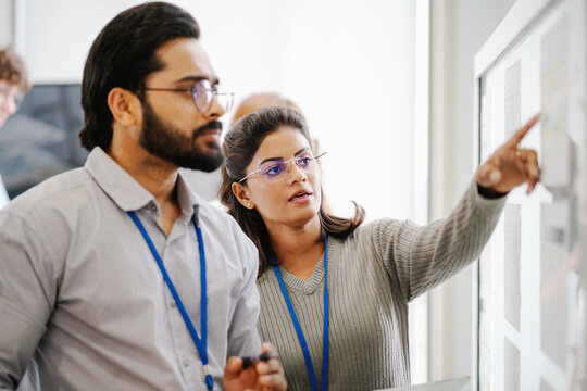 Business professionals working together in an office while analyzing information, discussing project plans, and pointing to data on a presentation board.