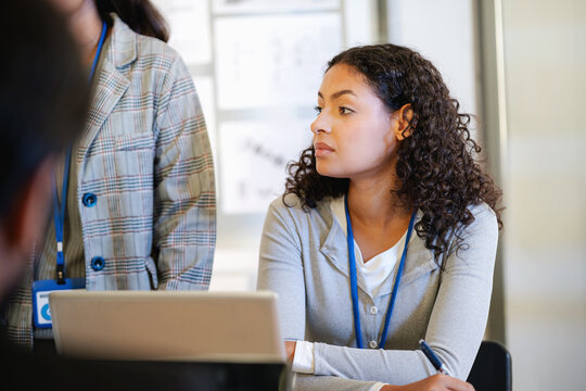 Female business professional working with a laptop during a workplace discussion, surrounded by colleagues in a modern corporate office.