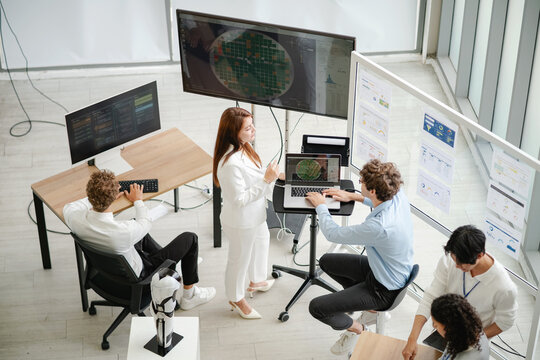 Diverse technology professionals collaborating around multiple computer screens and data dashboards while analyzing information and discussing business strategy.