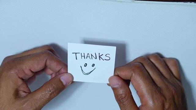 Person's hands unfolding a paper note with a thanks message and a smiley face on a white background