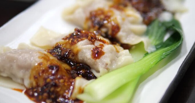 Close up of spicy Chinese wontons in chili oil with bok choy on white plate