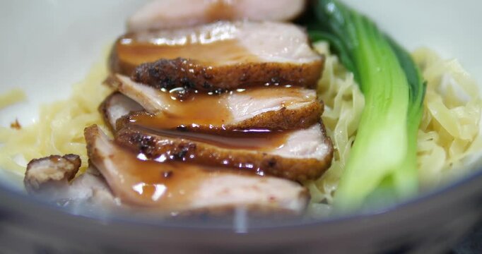 Close up of sliced roasted pork over flat egg noodles with sauce