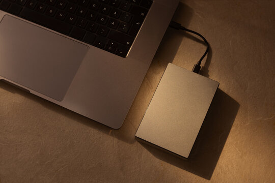 External hard drive connected to a laptop keyboard on a beige desk with warm lighting, showcasing modern data storage technology, file backup process, digital security, and stylish workspace.