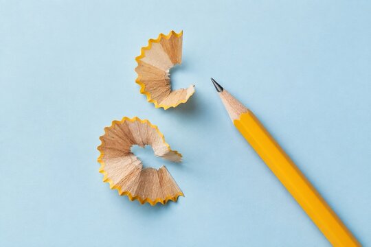 Sharpened yellow pencil and wood shavings on pale blue background