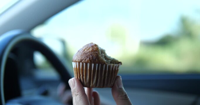 Close up of hand holding bitten banana muffin inside car