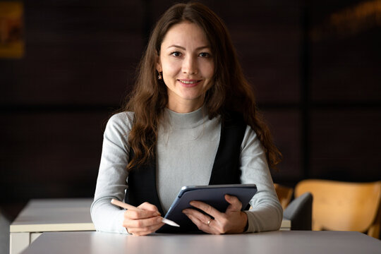 Smiling woman holding tablet and stylus at modern workspace, looking at camera with confident expression, showing digital work, technology, productivity and professional lifestyle