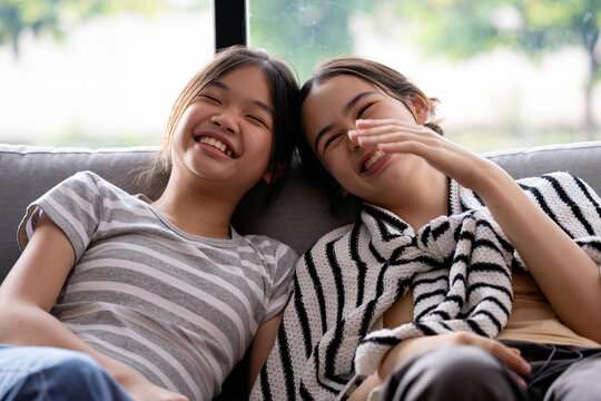 Two women laughing together on sofa at home, showing friendship, happy casual lifestyle, joy, relaxed conversation, comfort and cheerful bonding indoors