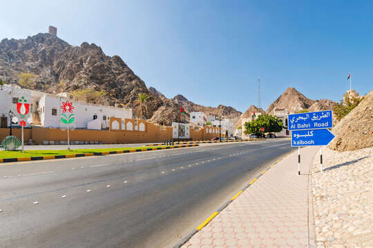Al Bahri Road in the Kalbooh area near Muscat Gate leading toward the corniche, with Al Marini Fort atop the Al Hajar Mountains and the Muscat Gate in the distance, in Muscat, Oman.
