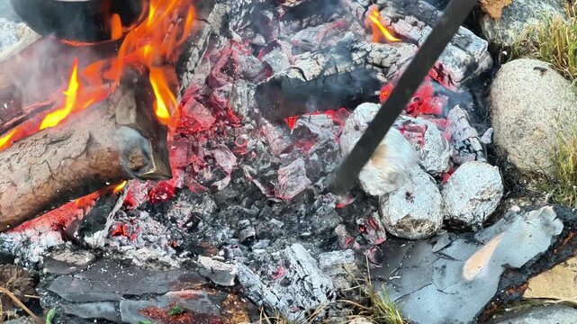 Close-up view of potatoes wrapped in aluminum foil cooking directly inside the hot glowing coals and embers of an outdoor campfire.