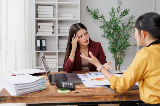 Businesswoman feeling stressed and frustrated during an intense discussion with a colleague in a modern office, experiencing a headache from workplace pressure and conflict