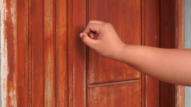 Close up of a person's hand knocking on a brown wooden home door.