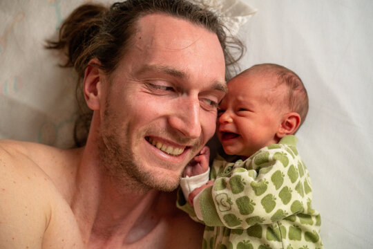 A happy grinning dad with his newborn baby girl crying