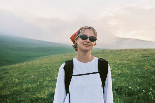 Hiker stands on green hillside with cloudy sky in background